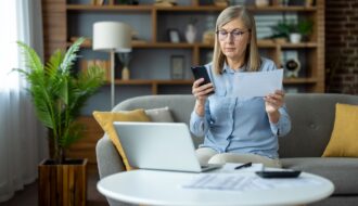 Mature woman managing finances at home with laptop and smartphone