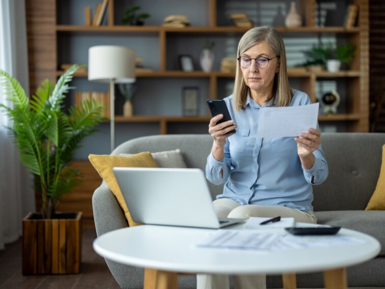 Mature woman managing finances at home with laptop and smartphone