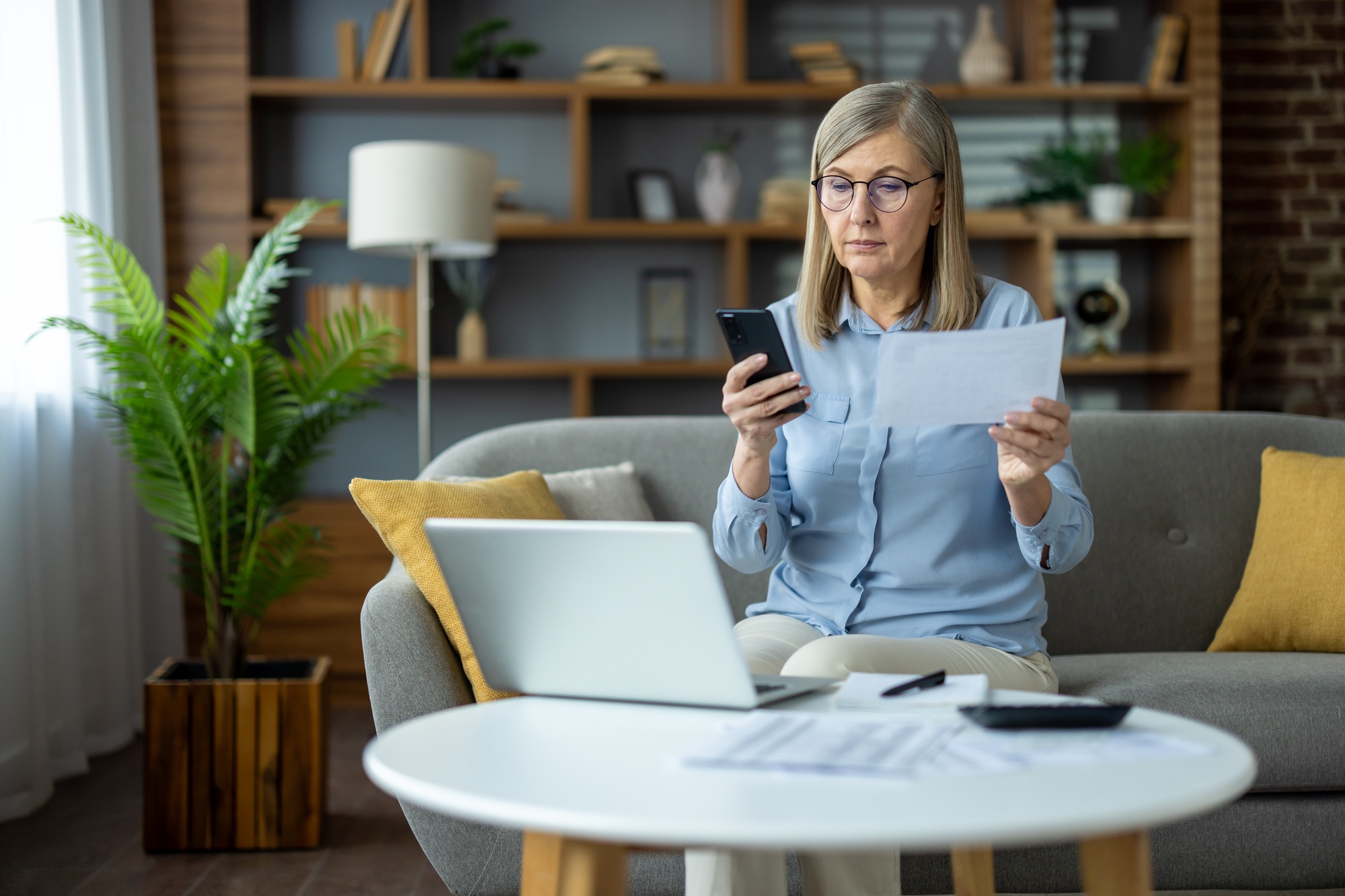 Mature woman managing finances at home with laptop and smartphone